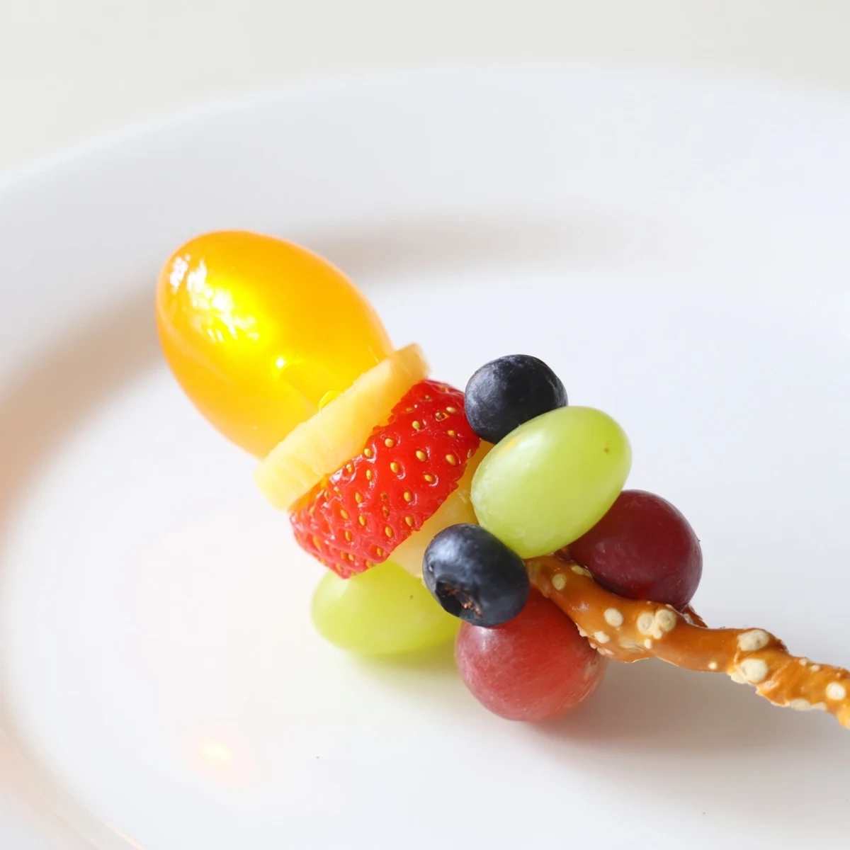 Colorful Christmas Light Fruit Skewers feature red, green, and yellow fruit threaded on a pretzel stick.