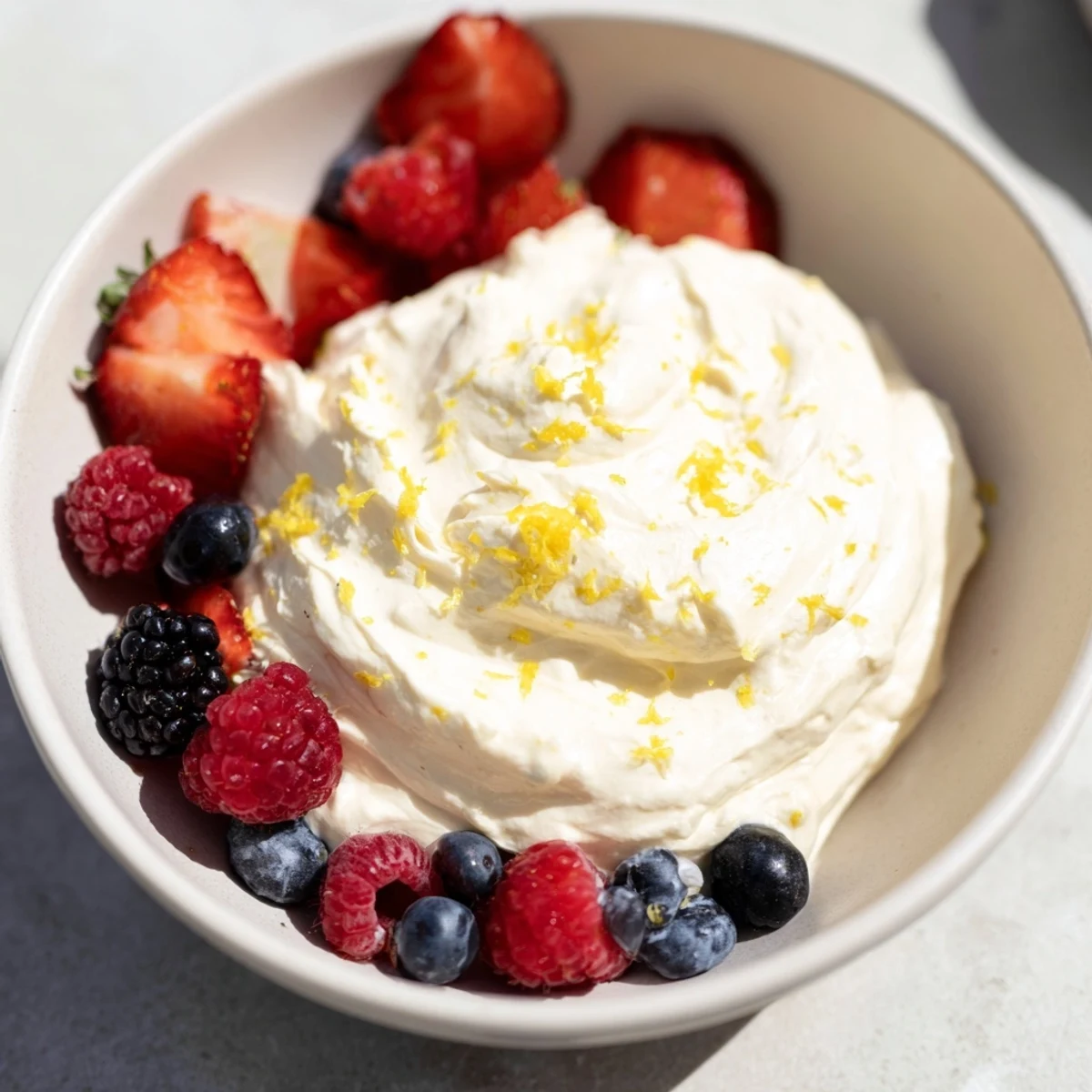 A bowl of delicious Fluffy Cream Cheese Fruit Dip surrounded by colorful strawberries and blueberries.