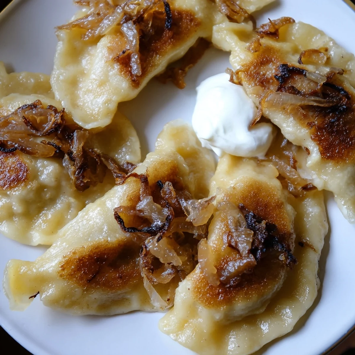 Golden-brown Polish pierogi dumplings filled with potato and cheese, served with sweet caramelized onions.