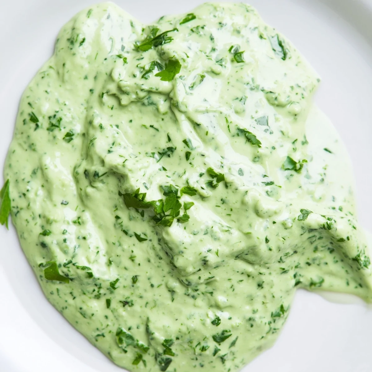 A jar of vibrant Green Goddess Dressing with a creamy, pale green texture, garnished with fresh chopped tarragon and parsley leaves.  