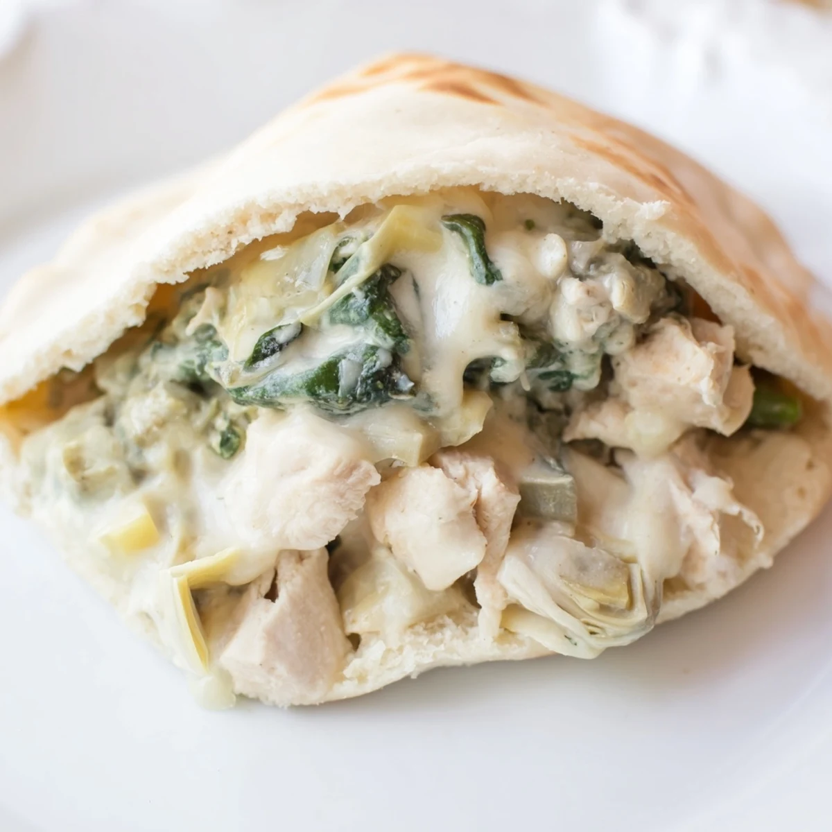 Freshly baked Spinach Artichoke Chicken Stuffed Pitas reveal a warm, savory filling of tender chicken, spinach, and artichokes.