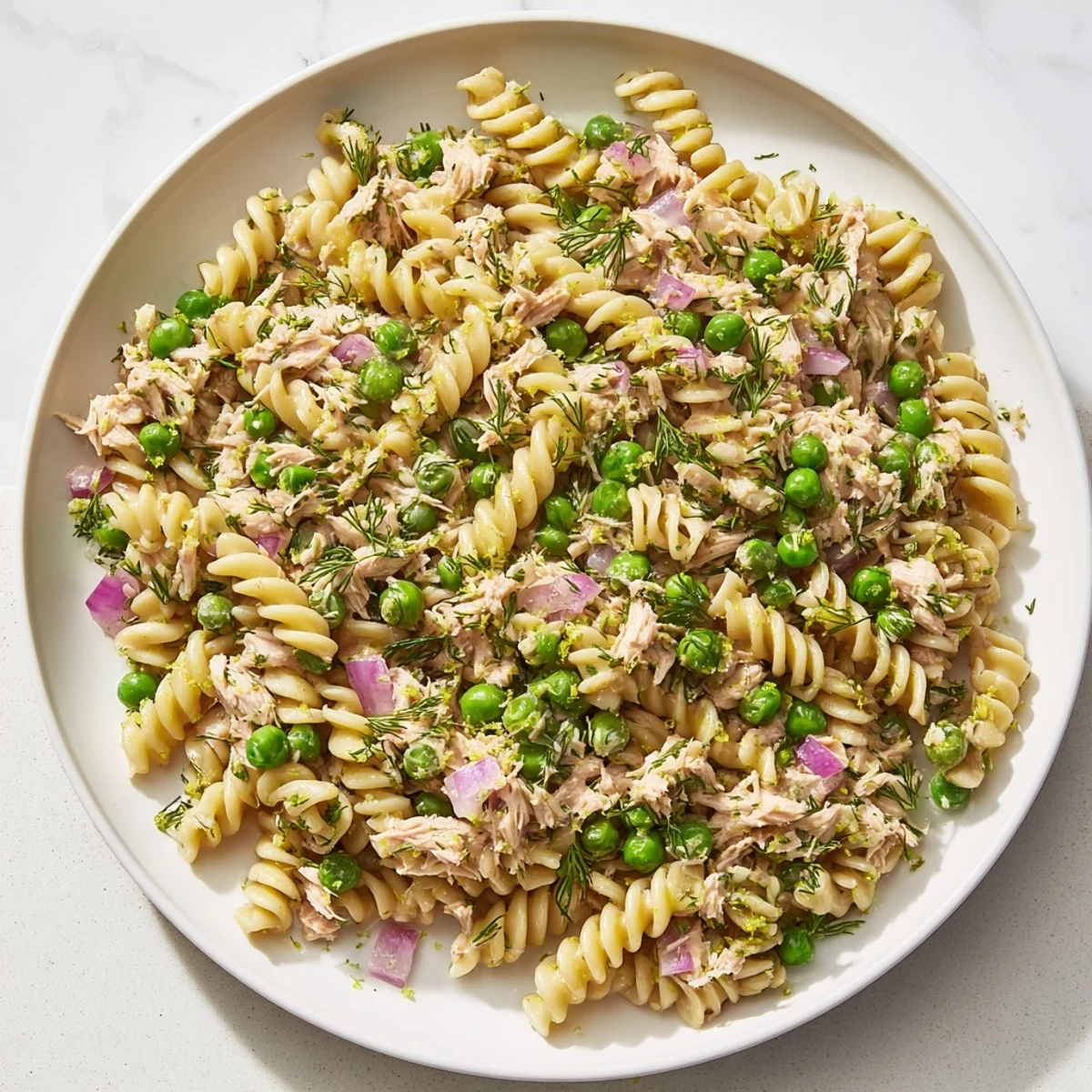 Fusilli pasta salad with flaked tuna, bright lemon zest, and fresh herbs in a white bowl.