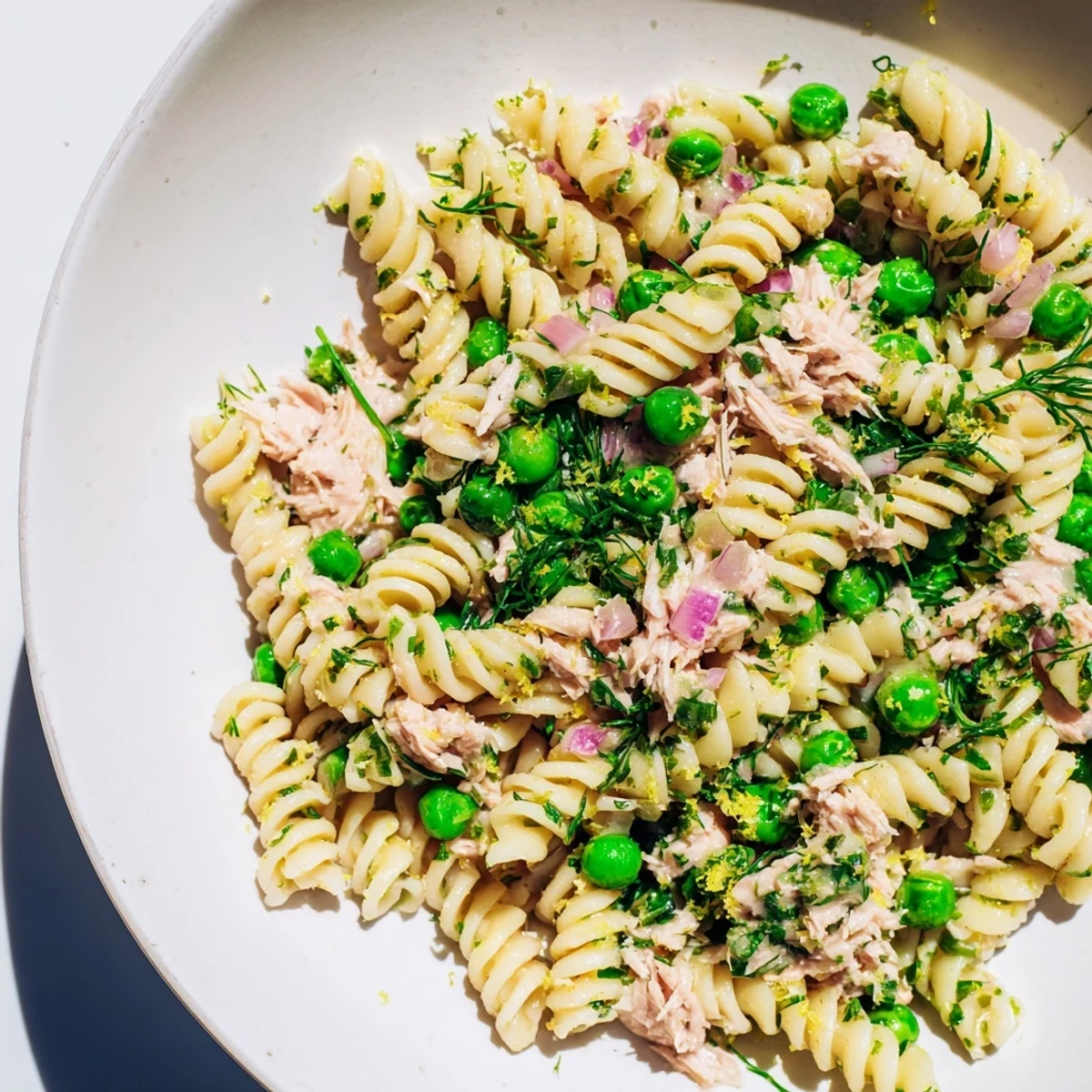 Cold Lemony Tuna Pasta Salad tossed with red onion and dill, garnished with lemon wedges.