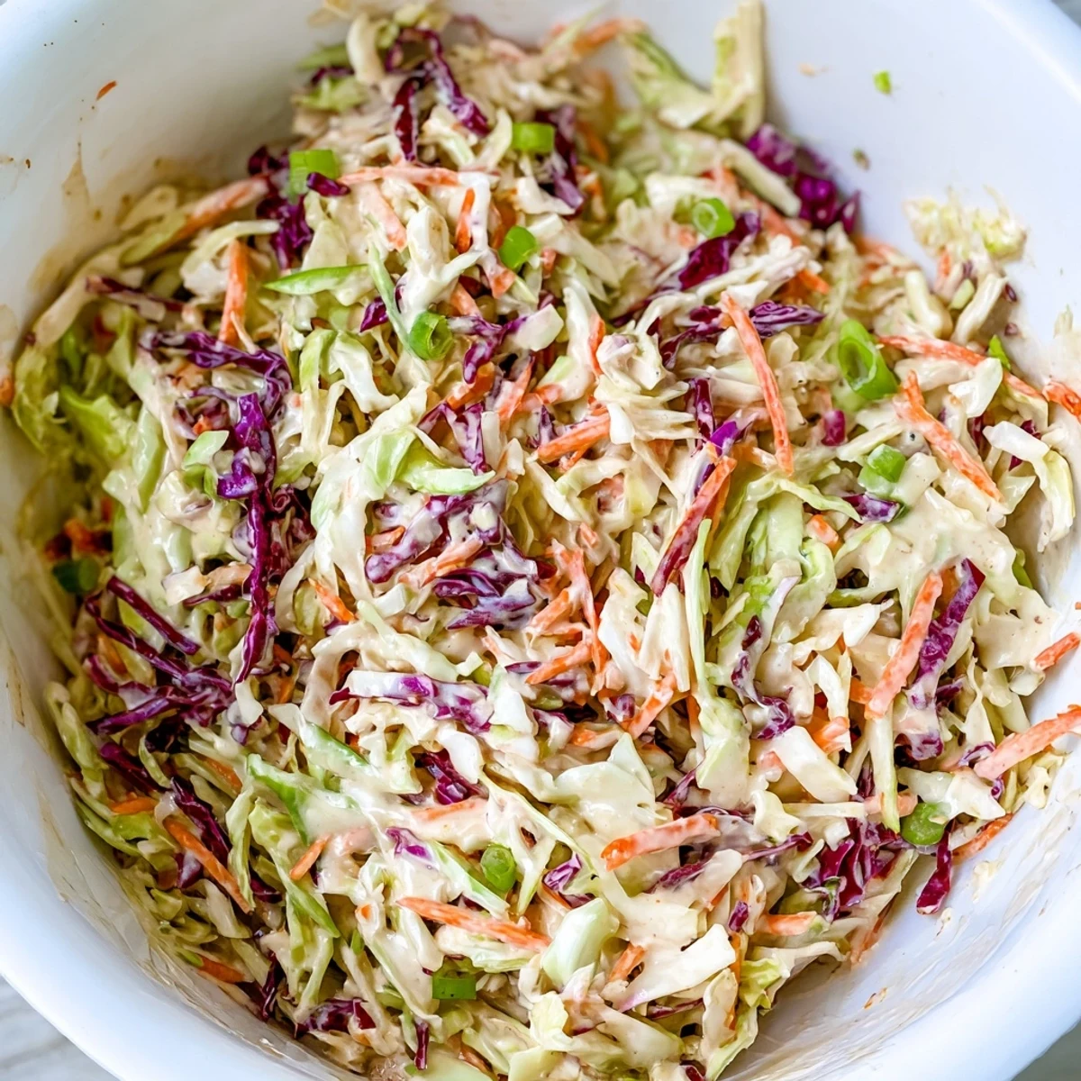A vibrant bowl of Best Cabbage Coleslaw topped with green onions, ready for a summer barbecue or picnic spread.  