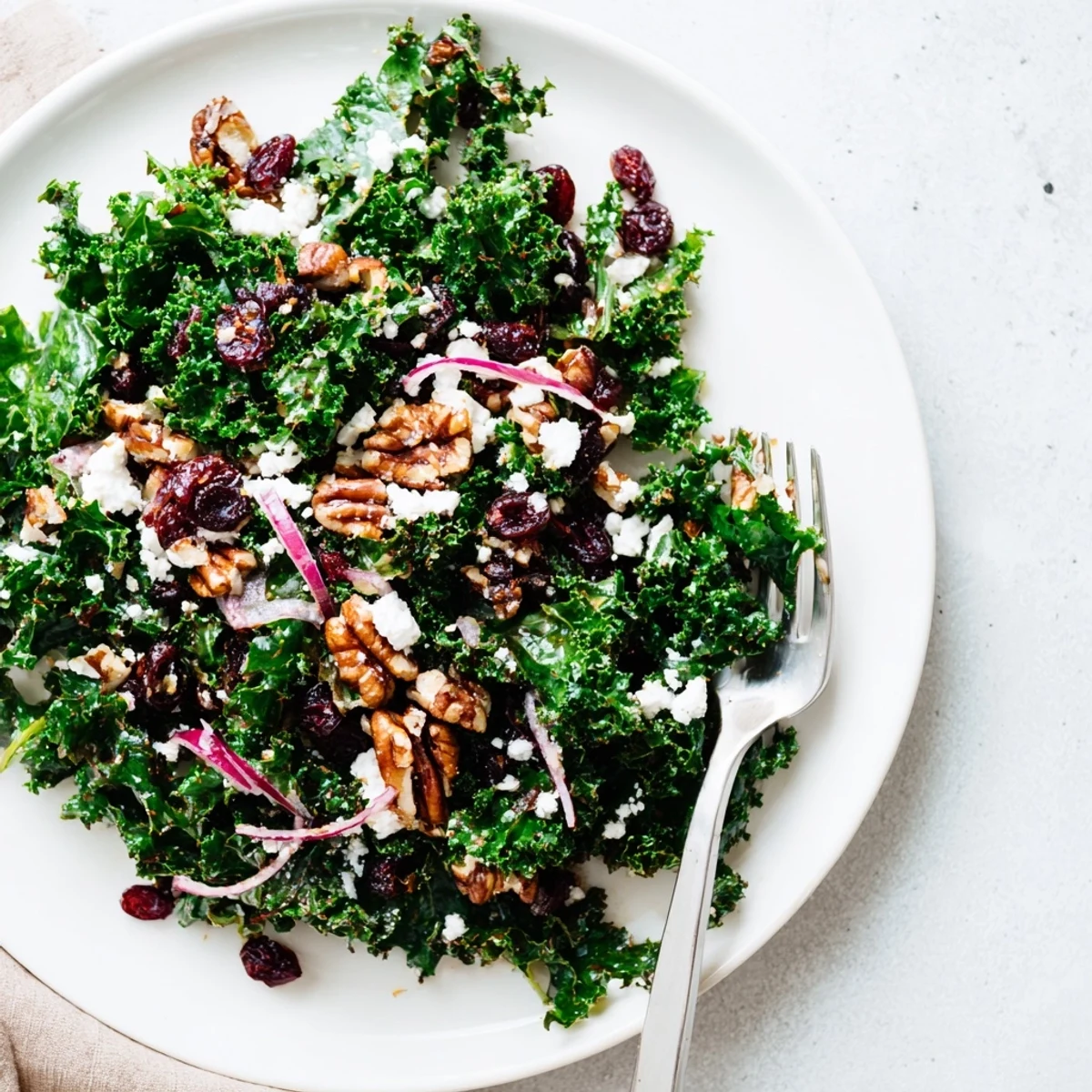 Hearty warm kale salad with maple mustard dressing includes sliced red onion, toasted walnuts, and dried cranberries, perfect for a quick vegetarian weeknight meal.