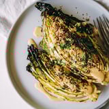 Golden-brown roasted cabbage wedges glistening with olive oil, arranged on a platter and generously drizzled with creamy tahini sauce and fresh herbs.