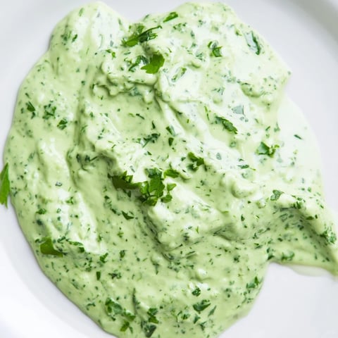 A jar of vibrant Green Goddess Dressing with a creamy, pale green texture, garnished with fresh chopped tarragon and parsley leaves.  