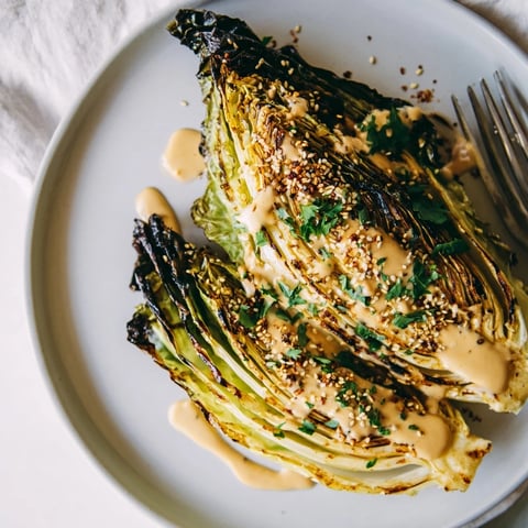 Golden-brown roasted cabbage wedges glistening with olive oil, arranged on a platter and generously drizzled with creamy tahini sauce and fresh herbs.
