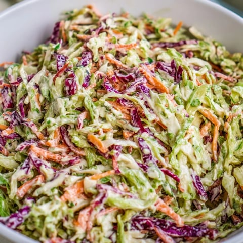 Freshly shredded green and red cabbage tossed with grated carrots in a creamy dressing, served chilled in a white bowl.  