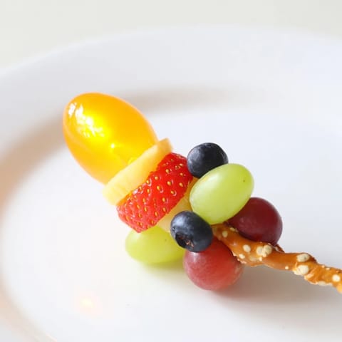 Colorful Christmas Light Fruit Skewers feature red, green, and yellow fruit threaded on a pretzel stick.