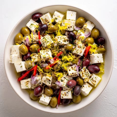 A close-up of Holiday Mix: Mixed Olives with Feta Cubes shows olives glistening in olive oil marinade.