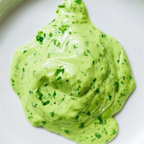 A bright bowl of Green Goddess Dressing surrounded by crisp vegetable crudités like cucumber slices, carrot sticks, and cherry tomatoes for dipping.  