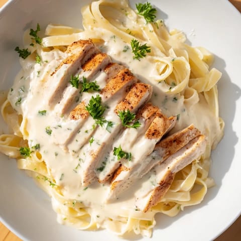 A close-up shows silky Alfredo sauce clinging to fettuccine and golden chicken in this Cajun Chicken Alfredo.
