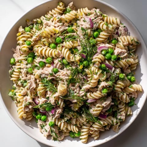Lemony Tuna Pasta Salad with peas and parsley, served ready to eat on a marble counter.