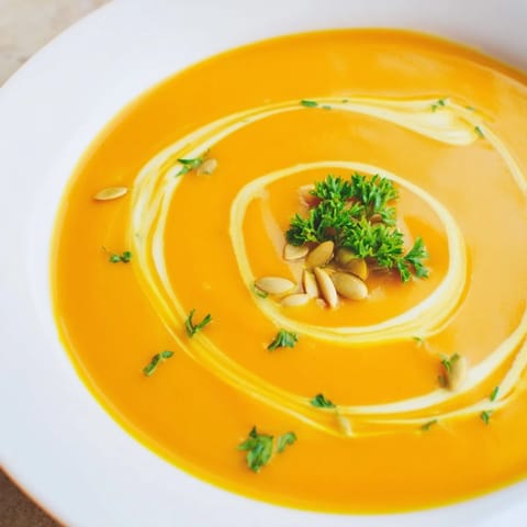Creamy, golden butternut squash soup in a rustic bowl, garnished with fresh parsley and toasted pumpkin seeds for a cozy fall lunch.
