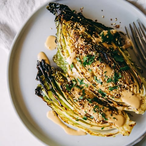 Golden-brown roasted cabbage wedges glistening with olive oil, arranged on a platter and generously drizzled with creamy tahini sauce and fresh herbs.