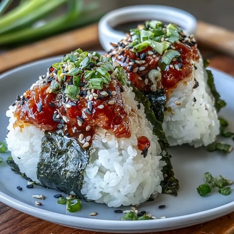 Hand-shaped rice balls filled with spicy tuna, wrapped in crisp nori, and garnished with sesame seeds for a flavorful snack.