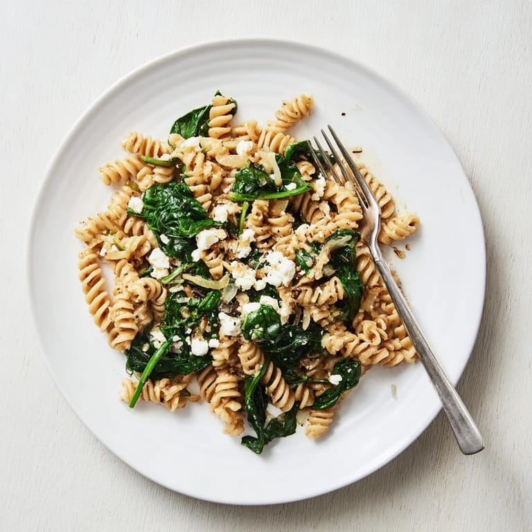 A bowl of Creamy Feta Spinach Pasta with melted feta sauce clinging to al dente pasta and wilted spinach.